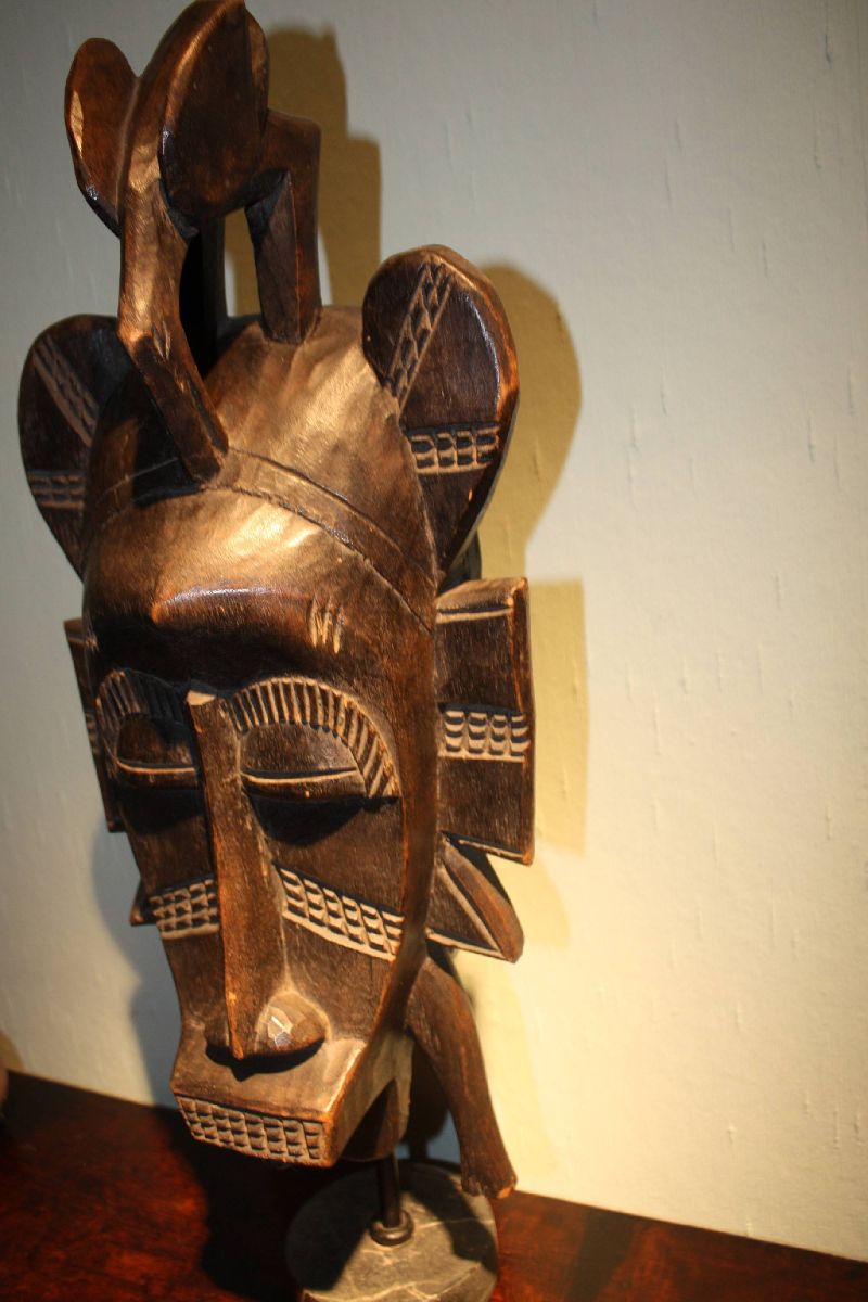 A large West-African handcarved wooden tribal Senufo ritual mask on a grey marble foot